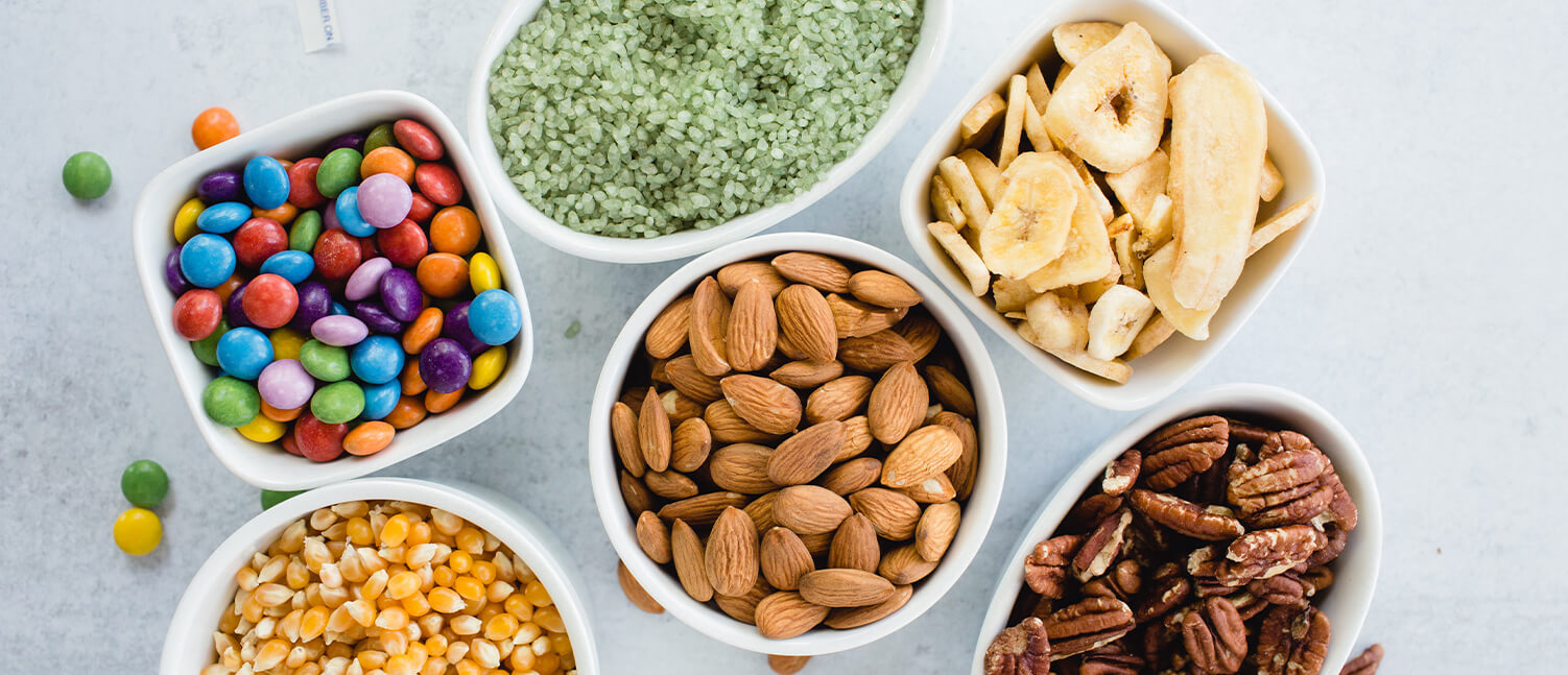 various bulk foods in different white containers including nuts, dried fruit, candy, popcorn, and grains.